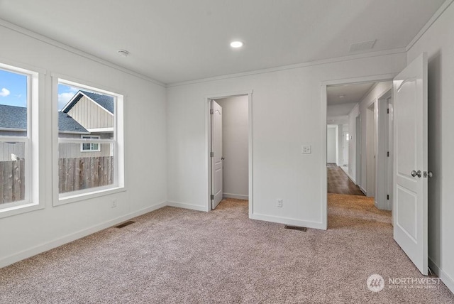 unfurnished bedroom with crown molding, a walk in closet, and light carpet