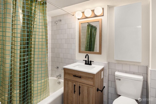 full bathroom featuring shower / tub combo with curtain, vanity, toilet, and tile walls