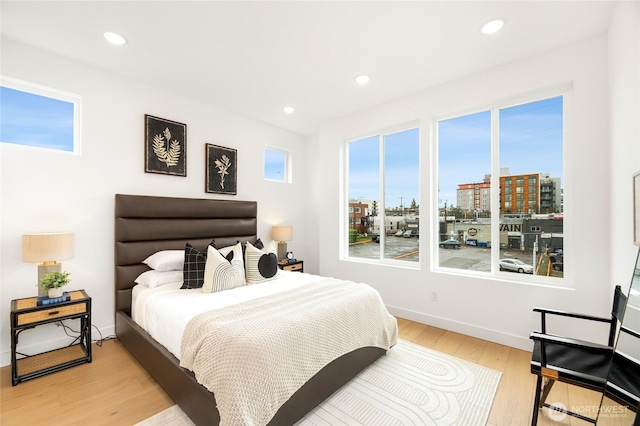 bedroom featuring light wood-style flooring, baseboards, recessed lighting, and a view of city
