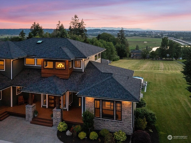 view of front of house with stone siding, covered porch, and a shingled roof