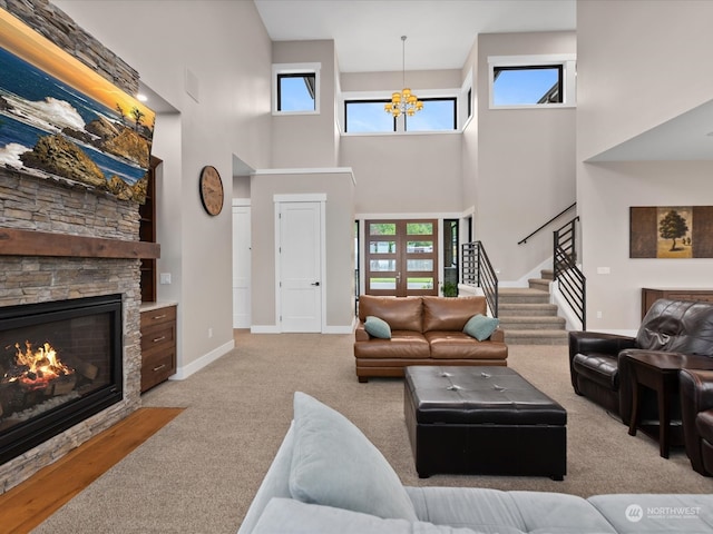 living room featuring stairway, carpet floors, a stone fireplace, baseboards, and a chandelier