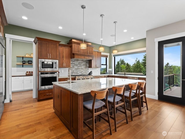 kitchen with a sink, light wood-style floors, appliances with stainless steel finishes, and an island with sink