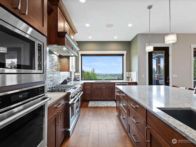 kitchen with pendant lighting, light stone counters, backsplash, wood finished floors, and stainless steel appliances