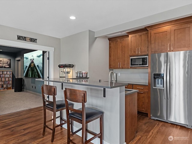 kitchen with dark wood-style floors, brown cabinetry, stainless steel appliances, dark countertops, and a kitchen breakfast bar