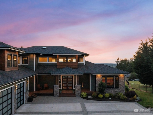 prairie-style house with fence, an attached garage, concrete driveway, french doors, and stone siding