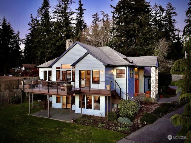 back house at dusk with a wooden deck and a patio