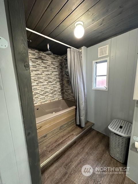 bathroom featuring hardwood / wood-style flooring, shower / bathtub combination with curtain, and wooden ceiling