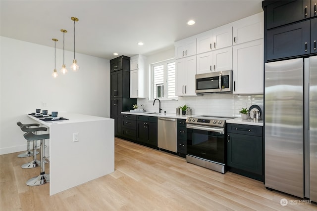 kitchen with appliances with stainless steel finishes, pendant lighting, sink, white cabinets, and a kitchen bar