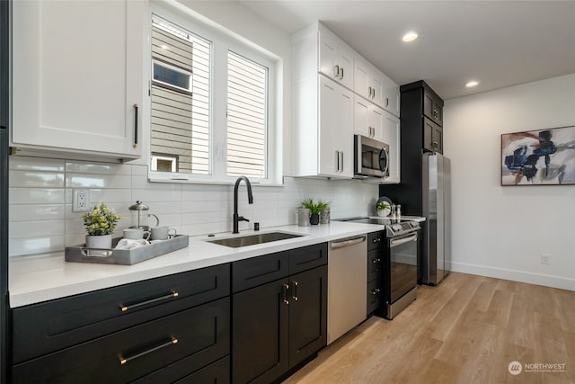 kitchen featuring sink, white cabinets, stainless steel appliances, light hardwood / wood-style floors, and backsplash