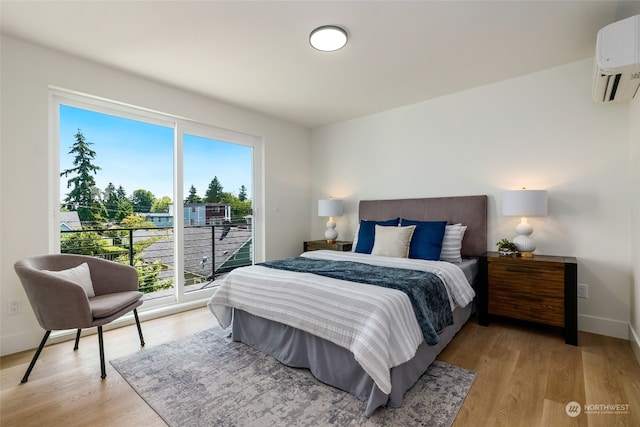 bedroom with a wall mounted air conditioner, light hardwood / wood-style floors, and access to outside