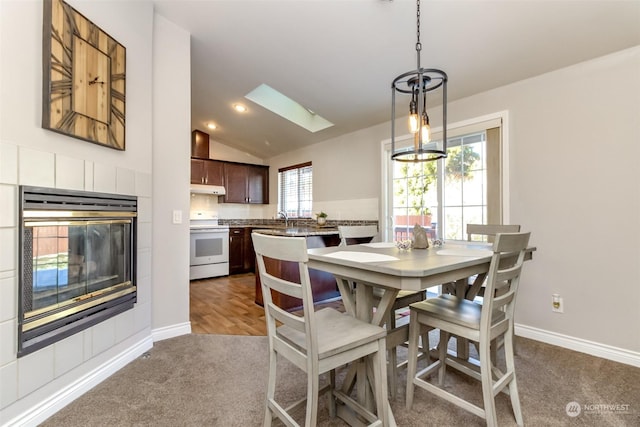 carpeted dining room featuring sink, vaulted ceiling with skylight, and a fireplace