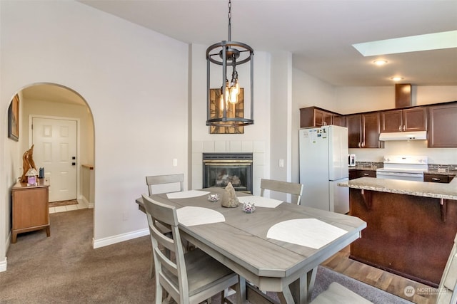 carpeted dining space featuring a tile fireplace and vaulted ceiling with skylight