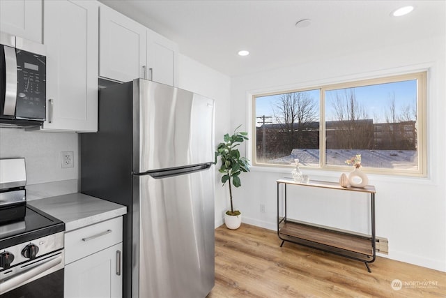 kitchen with white cabinetry, light stone counters, light wood-type flooring, and appliances with stainless steel finishes