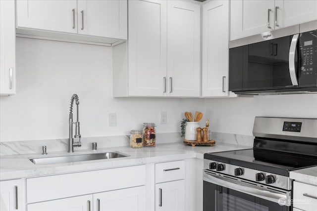 kitchen with stainless steel appliances, white cabinetry, sink, and light stone counters