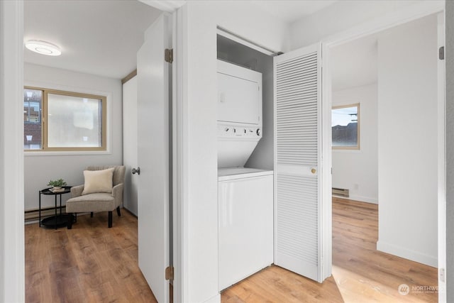 washroom with baseboard heating, stacked washer and clothes dryer, and hardwood / wood-style floors