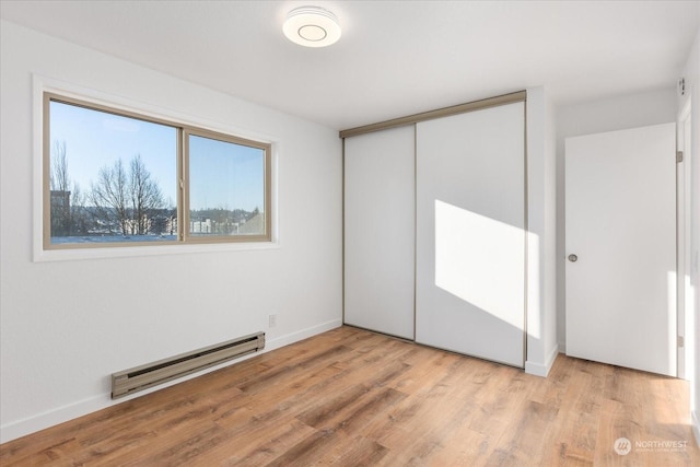 unfurnished bedroom featuring light hardwood / wood-style floors, a closet, and a baseboard heating unit