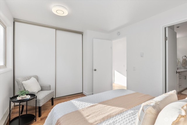 bedroom featuring ensuite bath, light wood-type flooring, and a closet