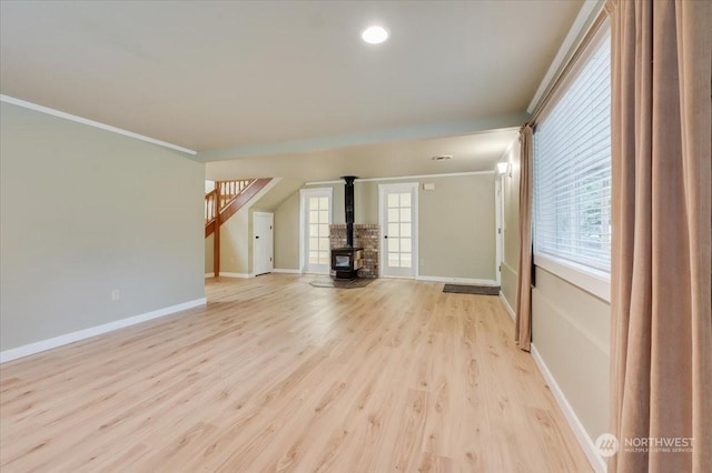 unfurnished living room featuring ornamental molding, a wood stove, and light wood-type flooring