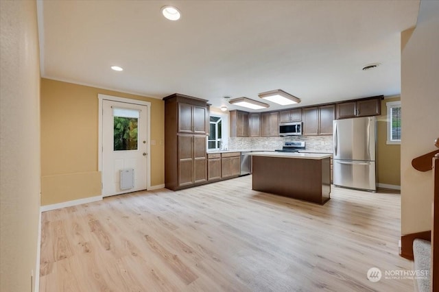 kitchen featuring light hardwood / wood-style flooring, appliances with stainless steel finishes, plenty of natural light, a center island, and decorative backsplash