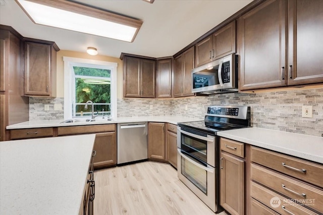 kitchen featuring sink, tasteful backsplash, dark brown cabinets, light wood-type flooring, and appliances with stainless steel finishes