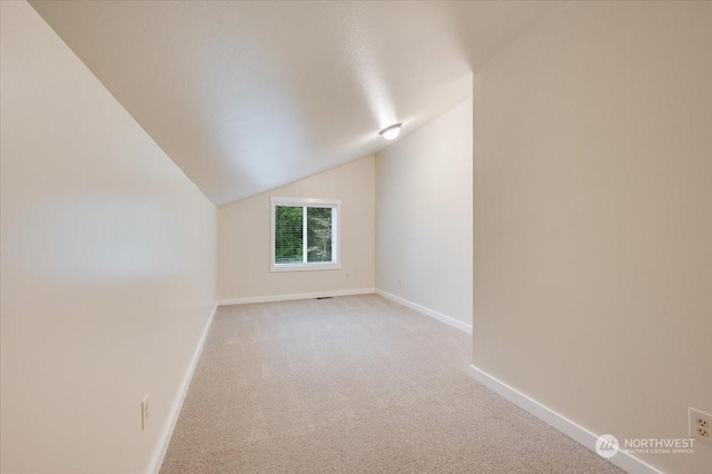 additional living space with light colored carpet and vaulted ceiling