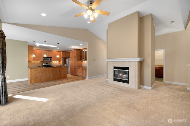 unfurnished living room with lofted ceiling, sink, a tile fireplace, ceiling fan, and light carpet