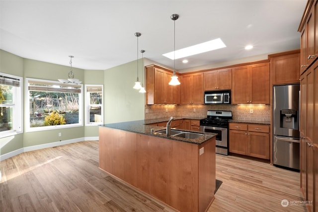 kitchen featuring sink, dark stone countertops, hanging light fixtures, stainless steel appliances, and decorative backsplash