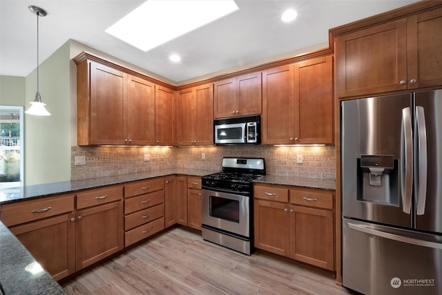 kitchen featuring appliances with stainless steel finishes, backsplash, a skylight, light hardwood / wood-style floors, and decorative light fixtures