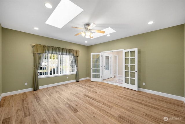 empty room with french doors, light hardwood / wood-style flooring, ceiling fan, and a skylight