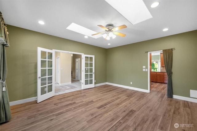 spare room with a skylight, ceiling fan, light hardwood / wood-style floors, and french doors