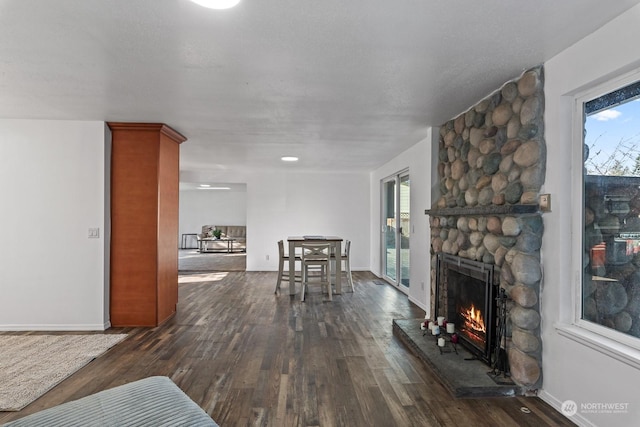 living room with dark hardwood / wood-style floors, a stone fireplace, and a wealth of natural light