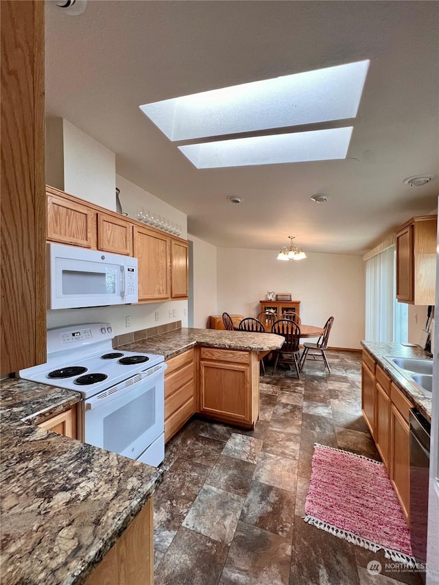 kitchen with a skylight, a chandelier, kitchen peninsula, pendant lighting, and white appliances