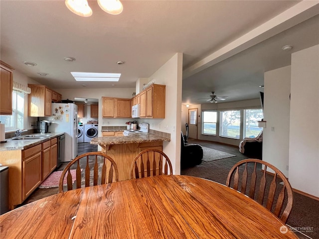 carpeted dining area with sink, a skylight, washing machine and dryer, and ceiling fan