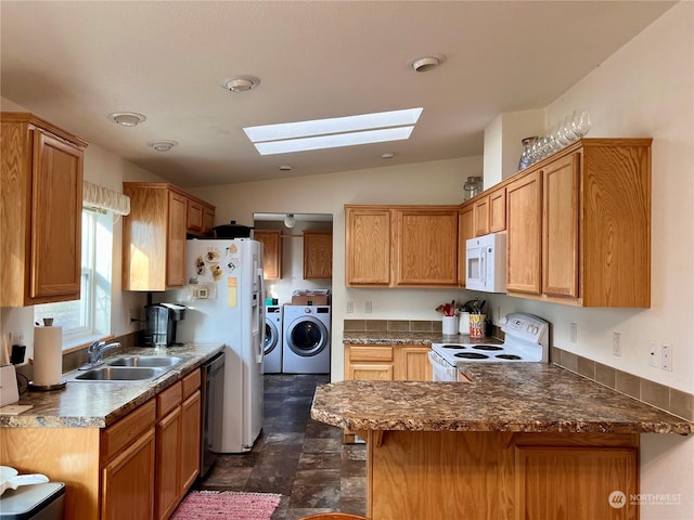 kitchen with vaulted ceiling with skylight, sink, white appliances, kitchen peninsula, and washer and clothes dryer