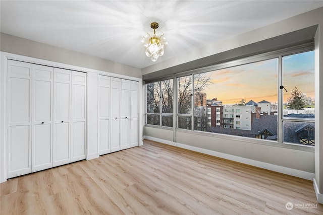 unfurnished bedroom featuring an inviting chandelier, two closets, and light wood-type flooring