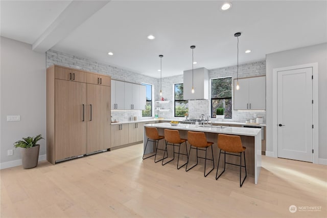 kitchen with white cabinetry, decorative light fixtures, an island with sink, and decorative backsplash