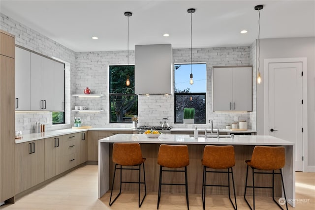 kitchen with hanging light fixtures, plenty of natural light, a center island, and wall chimney range hood