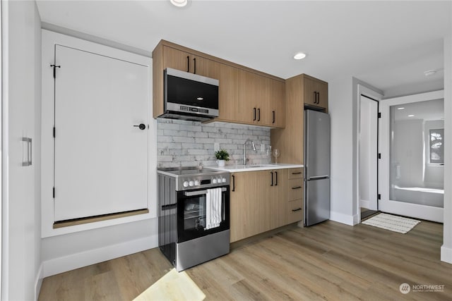 kitchen with sink, decorative backsplash, light hardwood / wood-style flooring, and appliances with stainless steel finishes