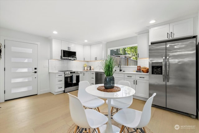 kitchen with decorative backsplash, stainless steel appliances, white cabinets, and light wood-type flooring