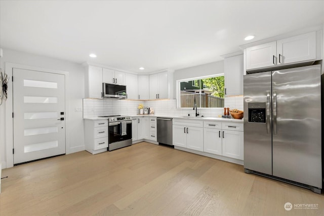 kitchen with sink, light hardwood / wood-style flooring, stainless steel appliances, white cabinets, and decorative backsplash