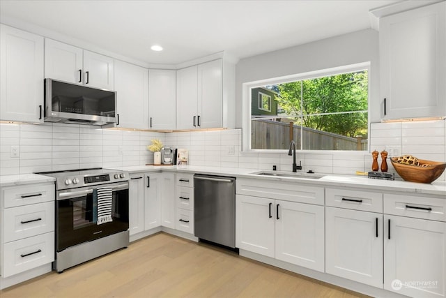 kitchen with sink, light wood-type flooring, white cabinets, stainless steel appliances, and backsplash