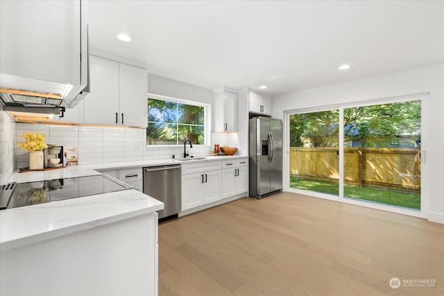 kitchen featuring white cabinetry, sink, light hardwood / wood-style floors, stainless steel appliances, and light stone countertops