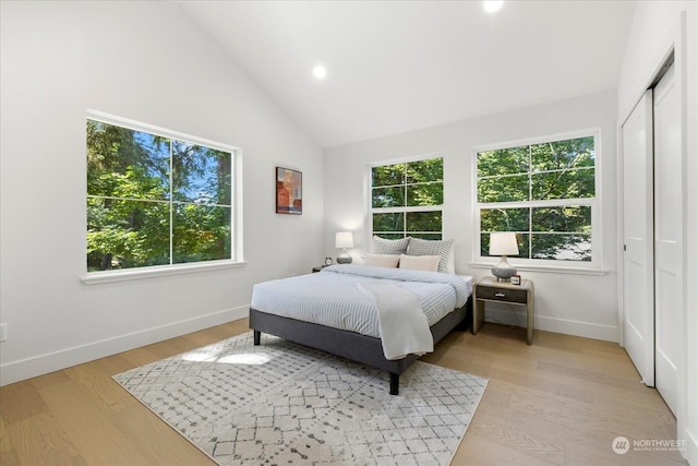 bedroom featuring multiple windows, a closet, high vaulted ceiling, and light hardwood / wood-style flooring