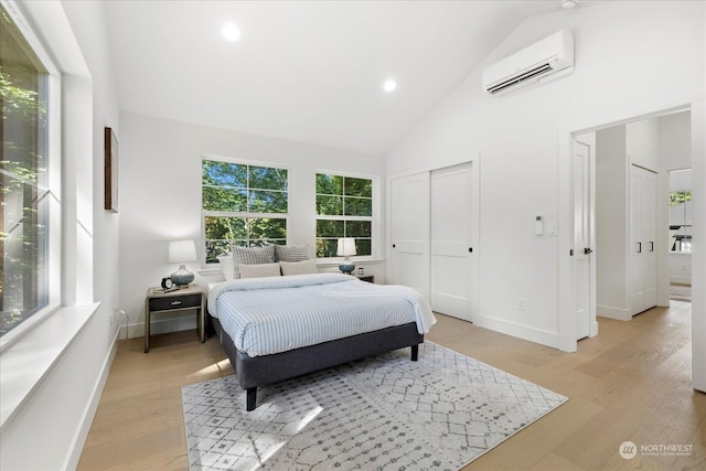 bedroom with high vaulted ceiling, light wood-type flooring, a wall unit AC, and a closet