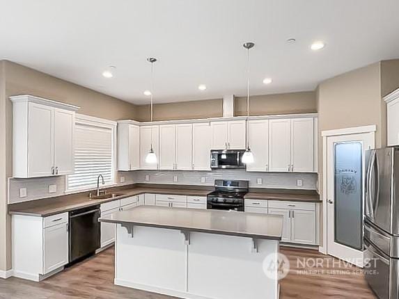 kitchen with appliances with stainless steel finishes, hanging light fixtures, and white cabinets