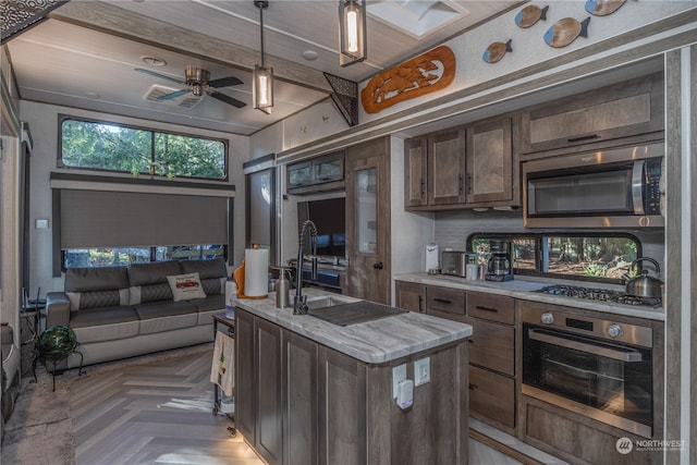 kitchen featuring decorative light fixtures, dark brown cabinets, parquet floors, appliances with stainless steel finishes, and a kitchen island with sink