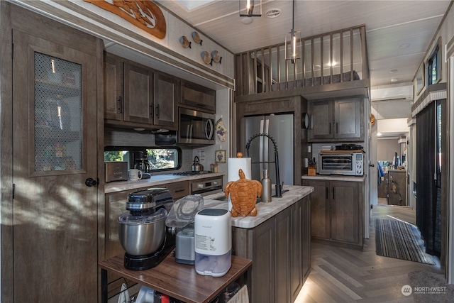 kitchen featuring stainless steel appliances, an AC wall unit, dark brown cabinetry, and decorative light fixtures