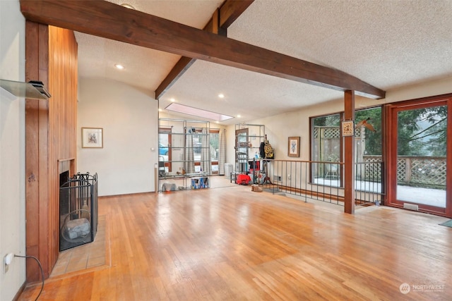 exercise area featuring vaulted ceiling, a large fireplace, a textured ceiling, and light hardwood / wood-style floors