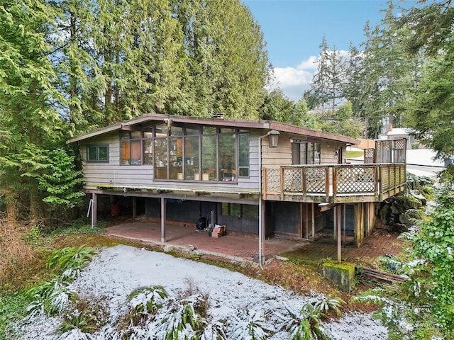 snow covered rear of property featuring a wooden deck, a sunroom, and a patio