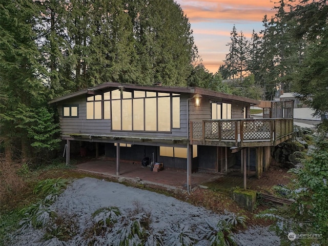 back house at dusk featuring a deck and a patio